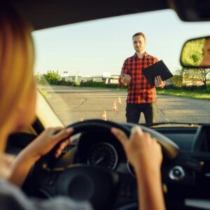 Woman in car, instructor with checklist on road