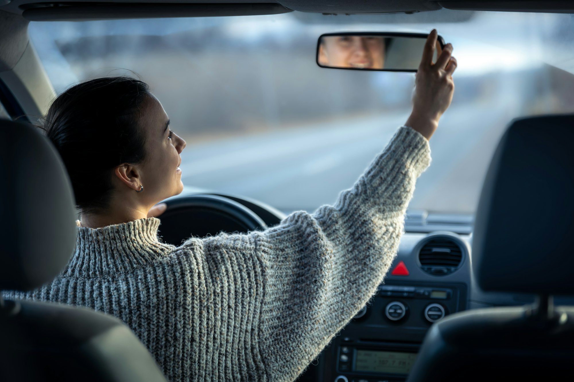 Happy young woman drives a car, inside view.