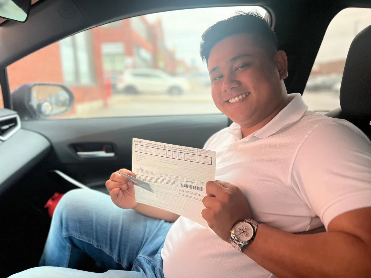 Student proudly holding driving license inside car after driving classes Oakville, North Oakville.