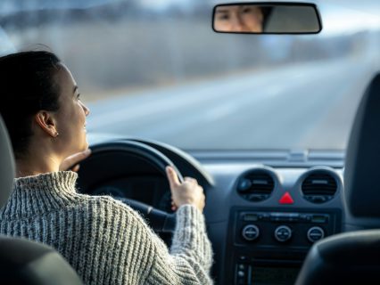 Happy young woman drives a car, inside view.