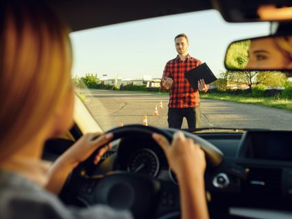 Woman in car, instructor with checklist on road